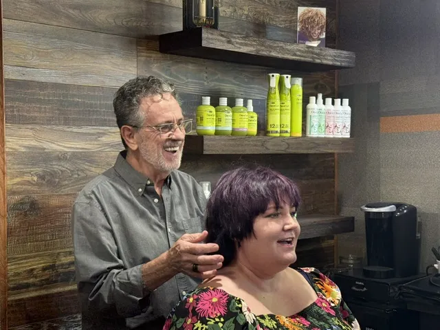 A stylist cuts hair for a smiling client in a salon setting.